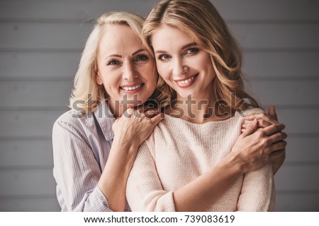 Beautiful senior mom and her adult daughter are hugging, looking at camera and smiling Royalty-Free Stock Photo #739083619