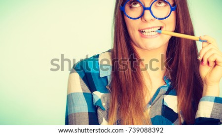 Studying, education and fun concept. Happy smiling nerdy woman in weird big glasses having idea and holding pen. Studio shot on blue background