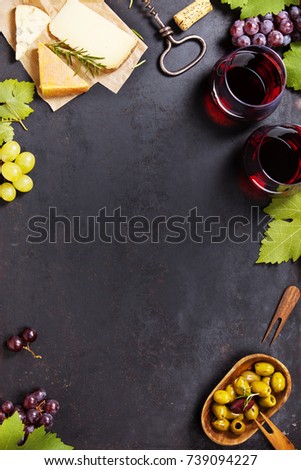 Wine and snack set. Variety of cheese, mediterranean olives, black and green grapes and glasses of red wine over dark background, top view, copy space