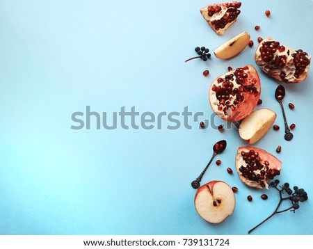 Juicy and raw fruits on a blue clean background. Pomegranate, pomegranate seeds, apple, wild grapes. Vintage spoons. Closeup. Space for text.