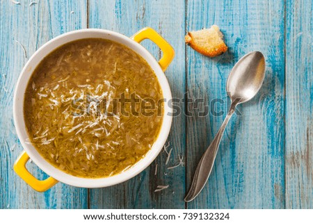 Classic onion soup with croutons. Served in yellow bowl on blue boards. Top view.