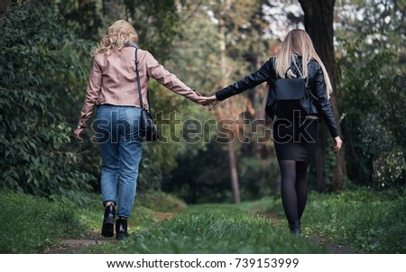 two beautiful lesbians in stylish clothes walking in the autumn garden