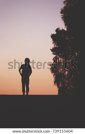 A little girl walking on a country road at evening. Black silhouette on sunset sky background.