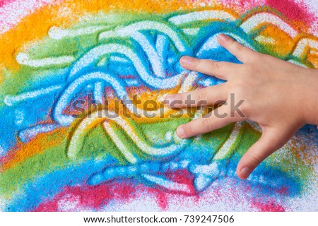 The child paints with colored sand on a white sheet