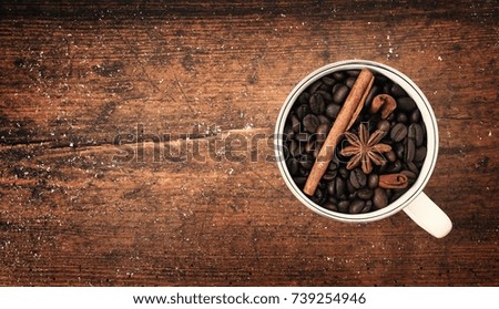 White cup of aroma coffee beans, cinnnamon and anise on old vintage wooden table.