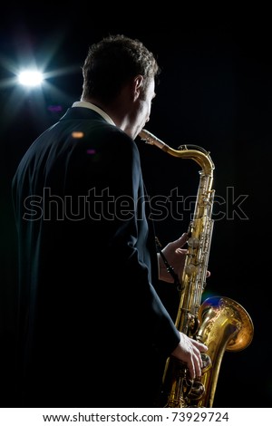 A jazz saxophone player facing the audience as he plays in a club - intentional flare Royalty-Free Stock Photo #73929724