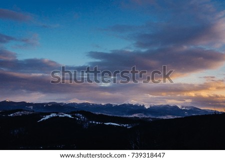 View of the snowy mountains. The nature of Carpathians. Landscape with forest, mountains and blue sky. Place for text and design. Evening, sunset. Winter.