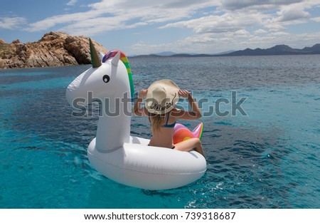 Girl named Viktoria is sitting on inflatable unicorn float in Emerald Coast of Sardinia.