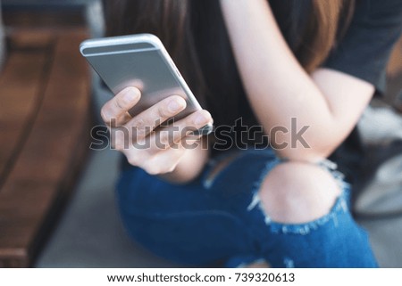 Closeup image of a woman's hand holding and using at smart phone sitting cross leg in modern cafe