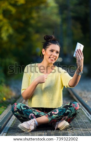Young girl siting and taking selfie on rails in park