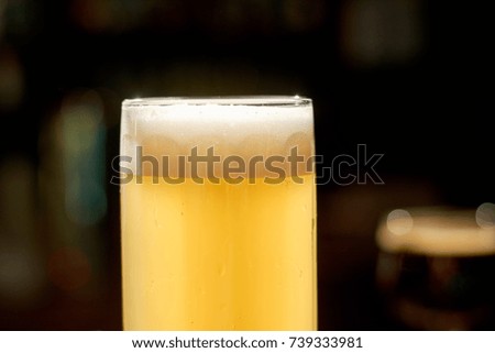 Cold lager beer on counter. Glass of fresh beverage with foam on dark bar background. Cropped image of glass with light beer.