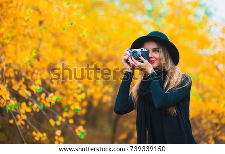 young woman photographing outdoors in autumn. Yellow leaves background