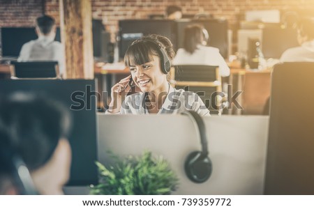 Call center worker accompanied by her team. Smiling customer support operator at work. Young employee working with a headset. Royalty-Free Stock Photo #739359772