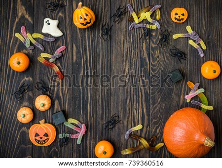Halloween background with pumpkin, candy and cookies. Top view of Hallowen objects on dark texture wooden table with space for text. Candy frame on vintage background for Helloween. Flat lay photo.