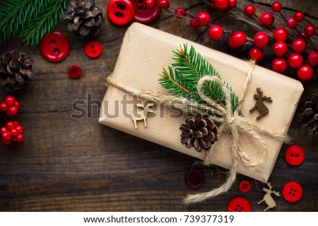 Christmas gift wrapped in kraft paper and tied with burlap twine decorated with red buttons, reindeer, fir branches and pine cones. Overhead view