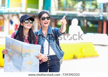 Hipster young girls wearing hat and sunglass with map, backpack enjoying colorful city. Tourist traveler on modern city view .Cute asian student college traveler feeling happy action with travel plan.