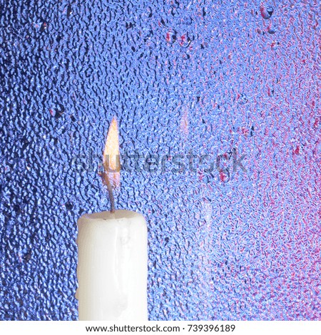 a burning candle on the background of a refracted glass