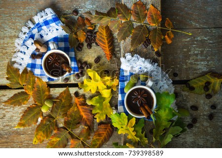 Autumnal concept with mup of coffee with spices, cinnamon stick and anise star on rustic wooden  background full of bright oak yellow leaves and acorns