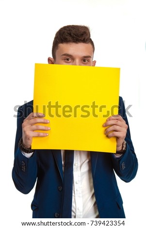 
Young guy in blue suit holding in hands yellow sheet of paper for notes and posing against white background