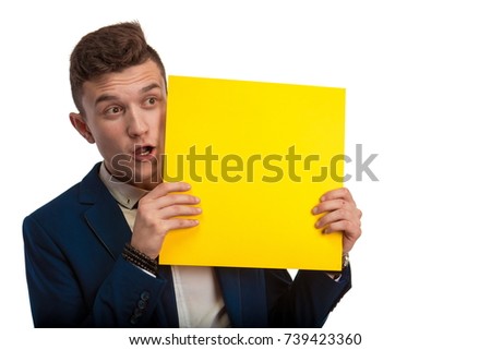 
Young guy in blue suit holding in hands yellow sheet of paper for notes and posing against white background