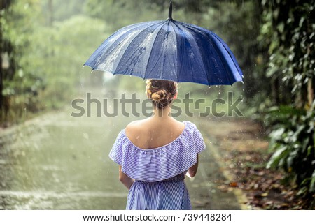 Beautiful young girl in dress with umbrella under the rain in the rain forest