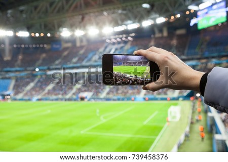 Fan hand with smartphone photographing football game