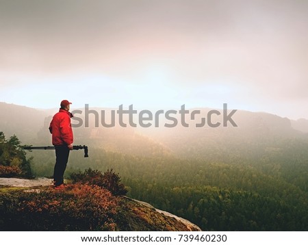 Photographer think about picture on peak  in the misty mountains. Photograph at daybreak above valley hidden in heavy mist.  Landscape view of misty autumn mountain hills and hiker silhouette