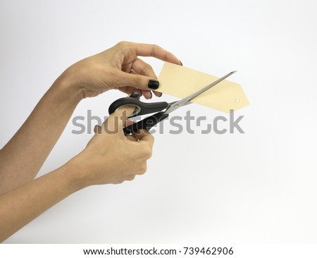 Female hand with black nails, holding scissors and cutting a price tag. Isolated on grey background.