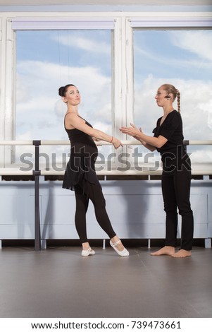 Pregnant woman ballet dancer and coach teach dance in ballet class