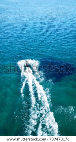 Aerial bird's eye view of jet ski cruising in high speed in turquoise clear water sea