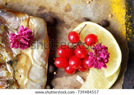 Grilled fish with cheese, honey, rowan, kalina, lemon slices, baked potatoes, pink flowers and spices on parchment paper