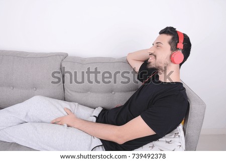 Attractive young man listening to music with headphones and relaxed on couch. Indoors.