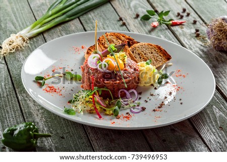 Delicious tartare with toasted bread and salad on a plate. Healthy lunch meal made of raw meat. Classical French cuisine. 