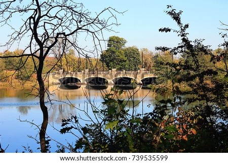 A stone bridge with four arches. Reflection in lake. Foliage, trees, grass, sky.