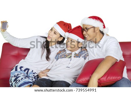 Picture of Asian family wearing Santa Claus hat while taking a selfie photo with a smartphone, isolated on white background