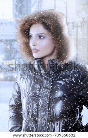 Picture of a beautiful Indian woman wearing winter jacket with fur under snowfall. Shot in the downtown