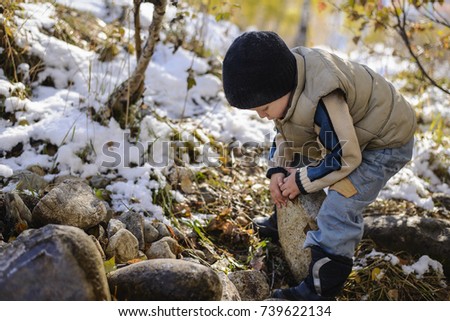 grimy warmly dressed child playing in autumn Park, picks up stones from the ground Royalty-Free Stock Photo #739622134