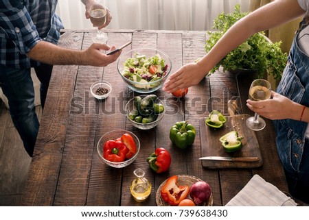 Husband takes pictures of how his wife is cooking dinner salad of vegetables on  wooden table in home kitchen