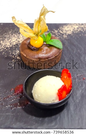 Detail on a dessert of molten chocolate coulant with vanilla ice cream strawberries, mint and golden berry