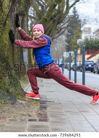 Outdoor sport exercises, sporty outfit ideas. Woman wearing warm sportswear training exercising, stretching legs outside during autumn.