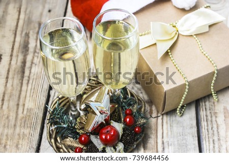 Happy new year, festive glass with champagne, gift box on the table in Santa Claus hat, Christmas decorations and scenery on the background. Picture for creating a greeting card, banner, postcard.