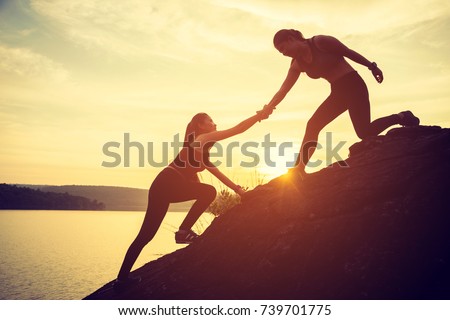 Hikers climbing on rock, mountain at sunset, one of them giving hand and helping to climb. Help, support, assistance in a dangerous situation Royalty-Free Stock Photo #739701775