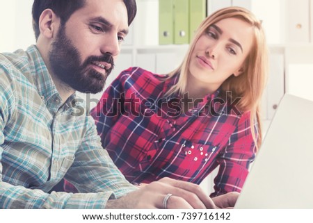 Two young designers wearing checkered shirts are sitting in a modern office and looking at a laptop screen. Concept of brainstorming and creativity. Toned image