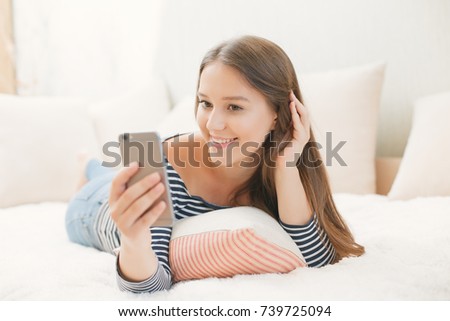 young girl in a bright room is lying on the bed with a phone