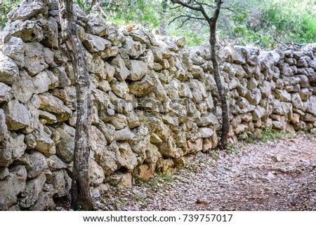 Stone rock fence or gabion and road or footpath. Old built rock wall structure and a path in the wilderness.