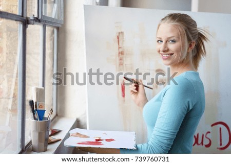 Portrait of young cheerful blonde female painter working in her atelier