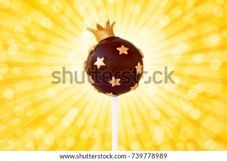 Chocolate cake pop king with crown, decorated with gold confectionery sprinkles In the form of star on a yellow background. Picture for a menu or a confectionery catalog.
