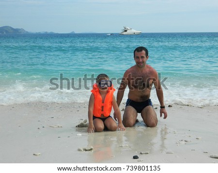 A beautiful picture, a man and a boy are sitting on the shore of the ocean, on an island, on white sand, and in the distance yacht and mountains