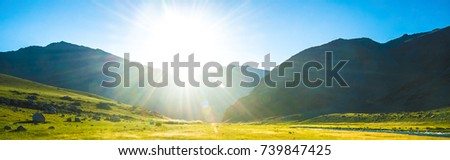 sun is coming up from over the hill, lighting up an lake down in valley.Grass,rocks and mountains also featured in the picture.green field, mountains and cloudy sky sunset. Beautiful landscape, grass 