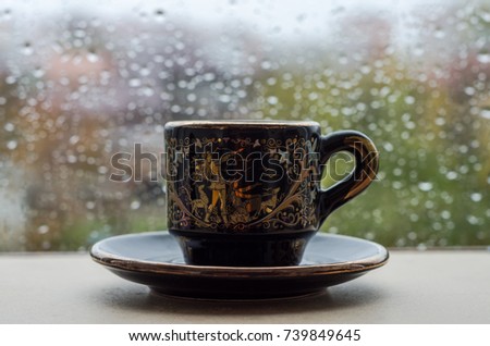 A cup of coffee on the window in the rain
